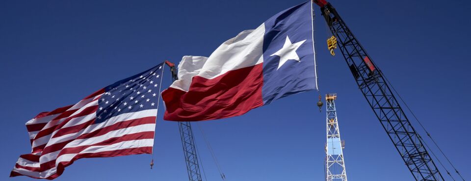 Photo of U.S. and Texas flags against a blue sky.