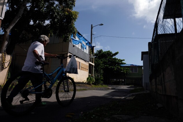 A woman walks by a house in Cataño, Puerto Rico, with a FEMA-provided blue tarp that was used to protect the roof damaged by Hurricane Maria two years prior, and is showing wear and tear, in September 2019.