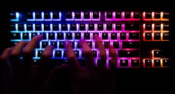 Photo of a man typing on a back-lit computer keyboard.